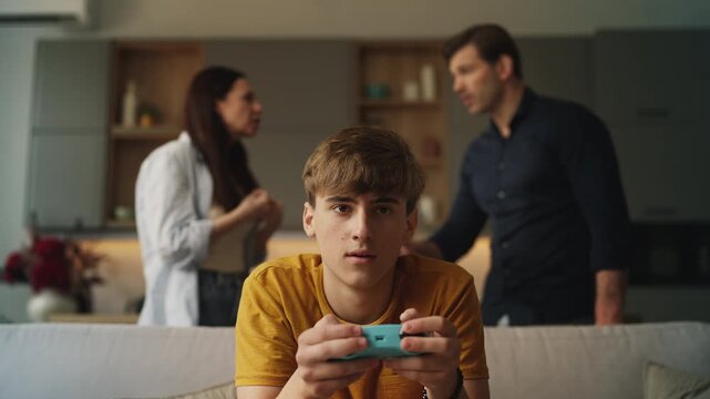 Teen boy playing video games while ignoring his displeased parents, family fight