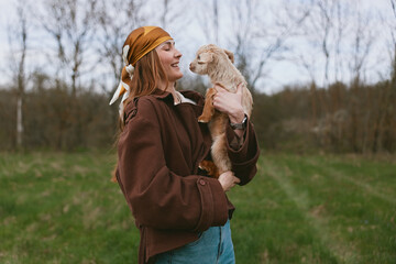 Fototapeta premium A joyful woman outdoors holds a fluffy animal close, smiling as they share a tender moment in a grassy field. A lifestyle portrait conveying warmth, connection, and affection between human and pet.