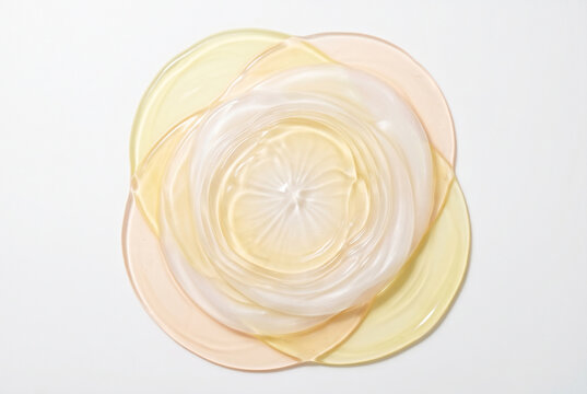 Circular shapes in soft colors are arranged in layers on a plain white background. The design creates a flower-like pattern. Light plays on the shapes, adding a subtle shine.