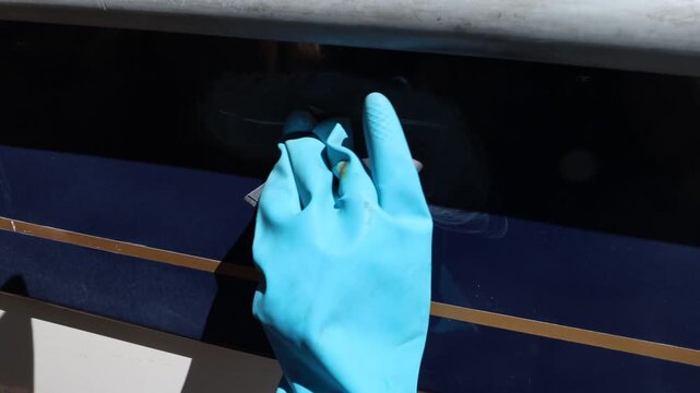Stockholm, Sweden A hand in a rubber glove polishes the hull of a blue motorboat tp try erase a scratch. 