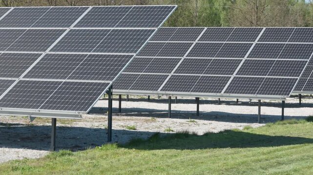Rows of bifacial photovoltaic solar panels at industrial renewable power plant. Ground mount installation on white gravel to maximize albedo and energy yield on sunny day outdoors.
