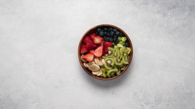 Stop motion fruit salad preparation in wooden bowl with apple banana kiwi and blueberries, top view on light background