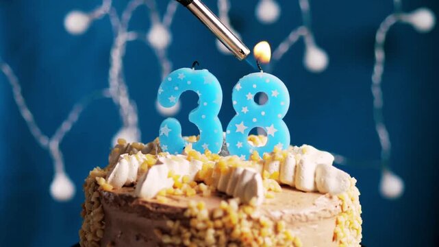 Birthday cake with a 38 number candle placed on a blue background captured in slow motion and close-up view shows a warm and elegant celebration moment. 