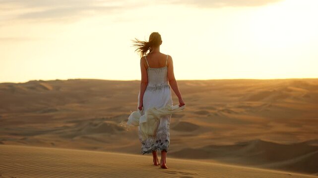 Female traveler at golden hour walk atop Huacachina sand dune, rear slomo view