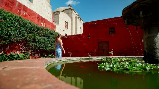 Young A female tourist explores the vibrant red walls and stone fountain of Santa Catalina Monastery in Arequipa, Peru. High-quality travel footage for tourism and architectural heritage themes