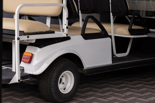 Side View of a Modern White Electric Golf Cart Parked on a Paved Area,A clean, modern white electric shuttle or golf cart with beige seating, parked on a brick-patterned walkway, ideal for luxury.