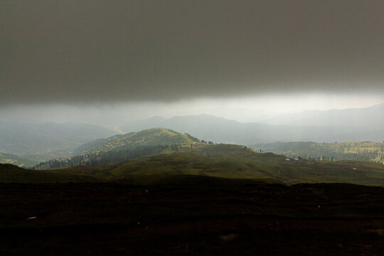 View of Ganga Choti peak with green rolling hills under dark heavy storm clouds and misty atmosphere in Bagh, Azad Kashmir, Pakistan.