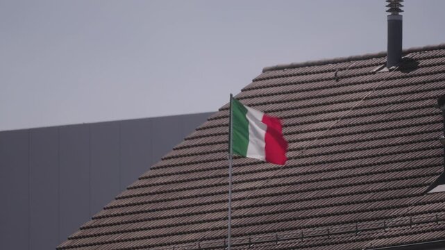 Italian flag waving with pitch roof in the background on a sunny spring day. Video shot May 8th, 2026, Zurich R&uuml;mlang, Switzerland.