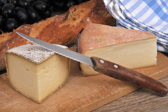 Morceaux de tomme de Yenne et de moelleux du Revard sur une planche &agrave; d&eacute;couper avec un couteau &agrave; c&ocirc;t&eacute; de pain et de raisin