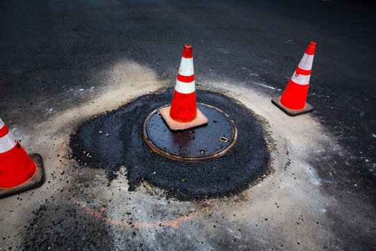 Road construction, a leak around a sewer manhole cover and traffic cones.