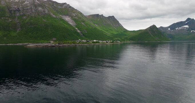 Remote fishing village of Hus&oslash;y on small island in &Oslash;yfjorden, surrounded by mountains on Senja, Norway. Aerial forward, copy space