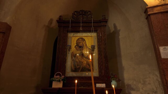Interior of Holy Trinity Cathedral in Tbilisi, Georgia. Features an illuminated Orthodox icon of Virgin Mary and Child, with several lit candles creating a warm devotional atmosphere for worshipers.