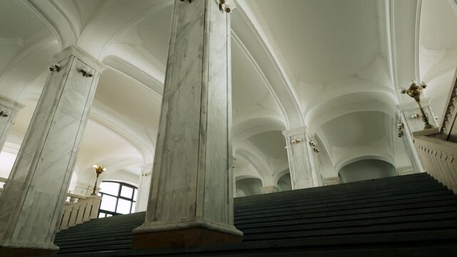 Soaring arched ceilings and majestic marble pillars define the interior of Holy Trinity Cathedral in Tbilisi, Georgia. A grand staircase leads upward, bathed in light.