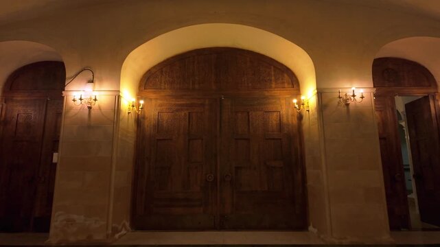 Grand carved wooden doors within the Holy Trinity Cathedral in Tbilisi, Georgia. Surrounded by architectural arches and illuminated by decorative wall sconces.