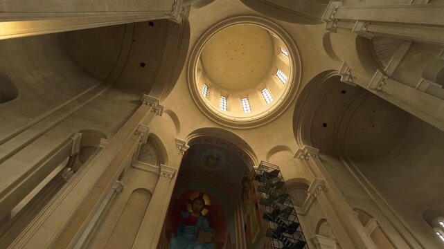Expansive interior view of the Holy Trinity Cathedral in Tbilisi, Georgia, capturing the grandeur of its dome, towering pillars, and vibrant religious frescoes decorating the walls and ceiling.