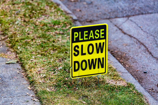 Please Slow Down sign on lawn between a sidewalk and the street