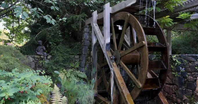 Waterwheel located at Butchart Gardens in Victoria,British Columbia, Canada.Rustic wooden waterwheel set against a stone wall surrounded by lush greenery.