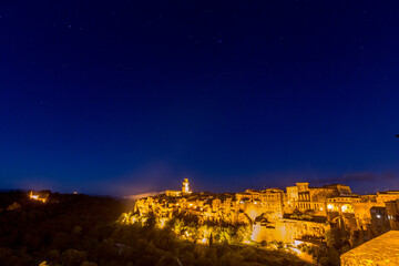 Obraz premium Nighttime view of town with a clock tower and stars in the sky, Sovana, Tuscany, Italy, long exposure motion blur