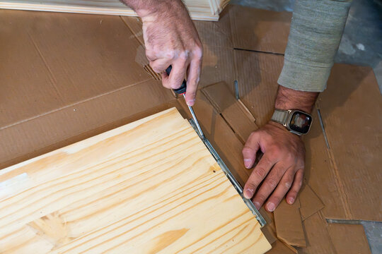 Male hands using a screwdriver to assemble wooden boards from a flat-pack box, concept of DIY furniture assembly and home project