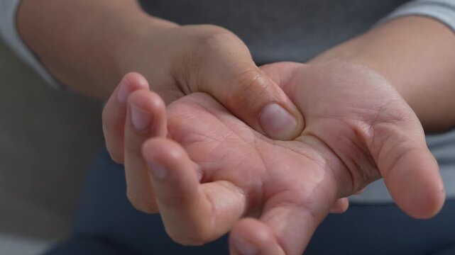 pain in hands and joints. woman feeling hand discomfort, rubbing and massaging wrist and fingers, performing warm-up exercises to alleviate pain, carpal tunnel syndrome, arthritis, or cramp symptoms.	