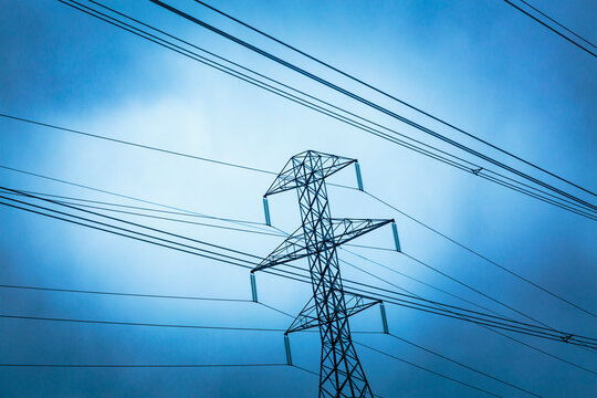 High transmission tower and wires seen from a low angle, overhead power cables.