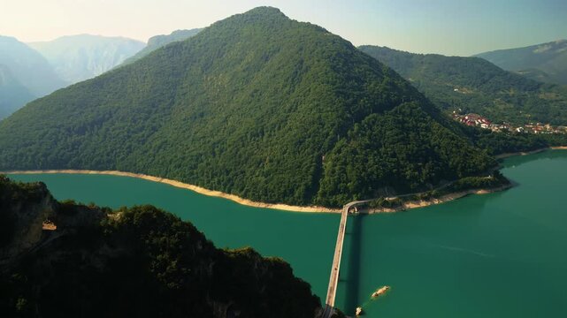 Cinematic aerial drone pull-back and pan shot revealing the bridge over Piva Lake. Stunning turquoise water and steep mountain slopes in Montenegro.
