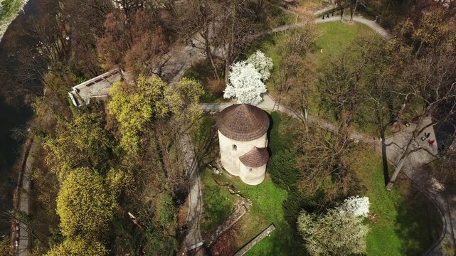Cinematic aerial drone orbital shot of the historic 11th-century Romanesque Rotunda of St. Nicholas in Cieszyn, Poland. Surrounded by green park and trees.