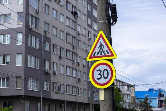 Pedestrian crossing warning sign and 30 km/h speed limit sign on a utility pole in urban area