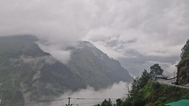 Mesmerizing timelapse video showing thick white clouds rapidly moving and swirling over a lush green mountain landscape.