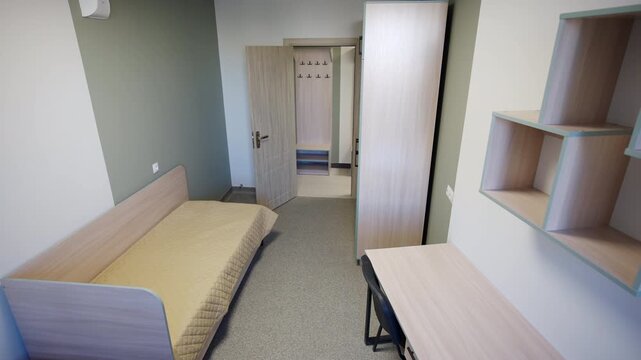 Complete residential room view shows single bed and wooden wardrobe. Study desk in addition to wall shelves maximize compact living space