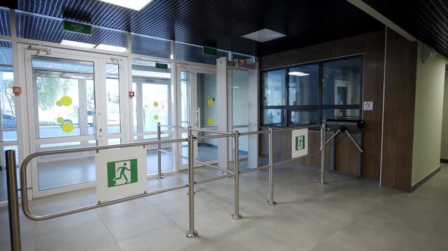 Secure entrance area features metallic turnstiles and glass exit doors. Lobby displays clear emergency signage along with safety barriers