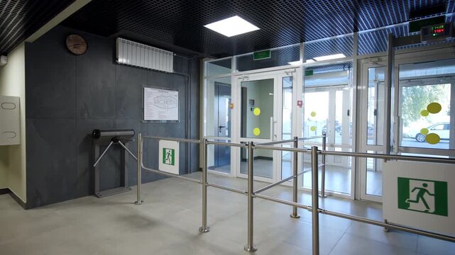 Metallic tripod turnstile and glass exit doors in entrance lobby. Checkpoint displays safety barriers for organized pedestrian flow