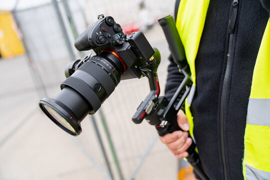 Videographer using a digital camera with a large lens and electronic steadycam system for high quality content production at a construction facility work zone