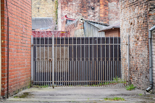 Metal gate between old brick buildings in narrow urban alley, showing secure access, industrial property, and redevelopment potential today on site