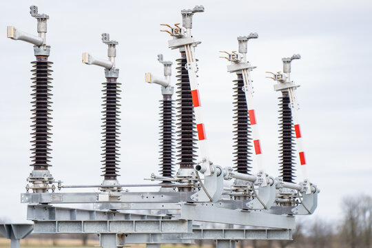 Electrical switchyard isolator bank with multiple porcelain insulator columns, red marked blades, and metal busbars for utility grid operations work