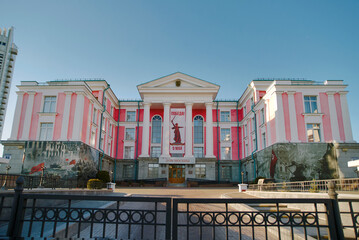Naklejka premium Minsk, Belarus. May 5, 2026. Dom Moskvy cultural center adorned with large scale war memorial paintings, Victory Day celebration banner between white columns during bright spring day, House of Moscow