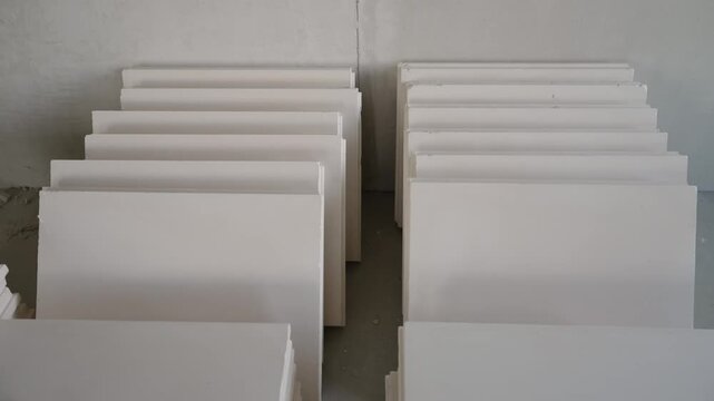 Stacks of white polystyrene insulation panels on concrete floor at building site. Minimalist composition with geometric shapes, neutral colors. Concept of construction, renovation, energy efficiency