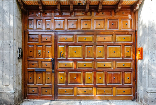 Gran puerta de madera maciza con patr&oacute;n sim&eacute;trico de casetones y llamador de le&oacute;n antiguo, textura arquitect&oacute;nica r&uacute;stica