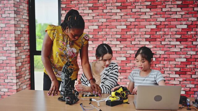 Female teacher helping two young girl students building a robotic arm in a STEM education coding class