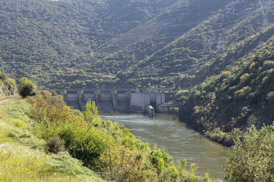 View of the Douro River dam and hydroelectric power station nestled between steep green hills and lush Mediterranean vegetation in Portugal.