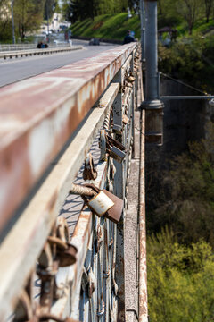 View of rusty metal bridge railings adorned with numerous love locks overlooking a deep green canyon and a road Kamianets-Podilskyi, Khmelnytska Oblast, Ukraine.