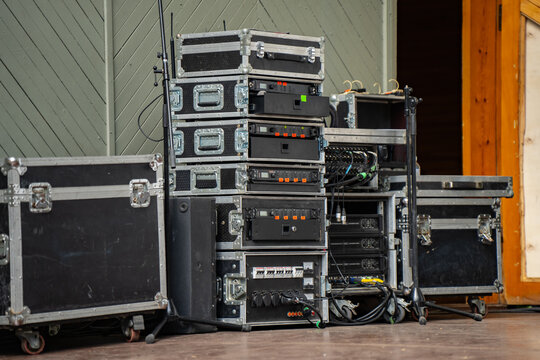 Professional sound equipment and audio rack cases stacked on an outdoor stage for a live concert event featuring power amplifiers and wireless microphone receiver units