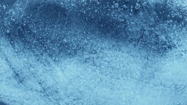 Extreme macro close-up of cracked blue melting ice texture in time lapse. Abstract frozen water surface with translucent crystal patterns, condensation and thawing details in studio lighting.