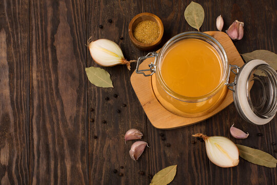 Traditional homemade beef bone broth with vegetable in glass jar on dark rustic wooden background.
