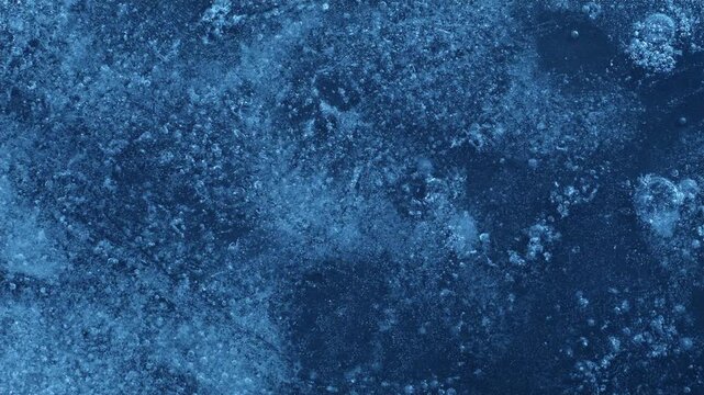 Extreme macro close-up of cracked blue melting ice texture in time lapse. Abstract frozen water surface with translucent crystal patterns, condensation and thawing details in studio lighting.