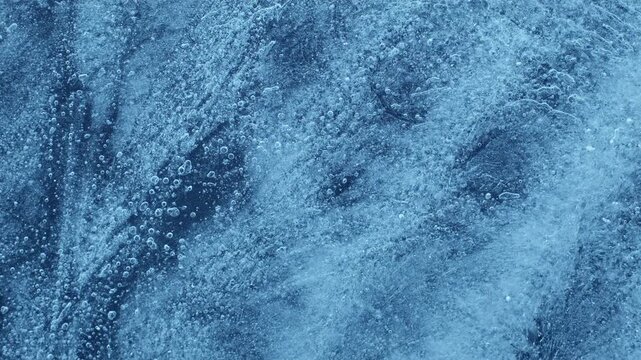 Extreme macro close-up of cracked blue melting ice texture in time lapse. Abstract frozen water surface with translucent crystal patterns, condensation and thawing details in studio lighting.
