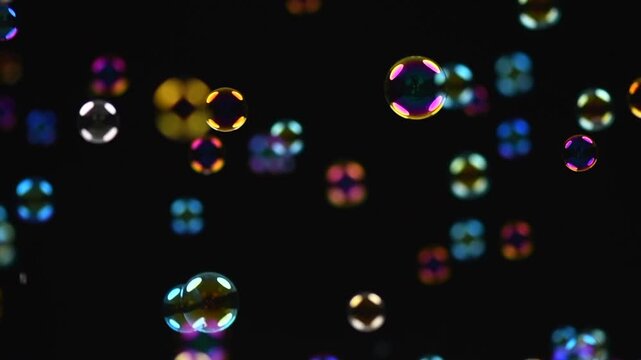 Soap bubbles isolated on black background. Holiday backdrop with flying colorful soap bubble, close up. Abstract Holiday background for screen using, slow motion. Birthday celebrating, party. 