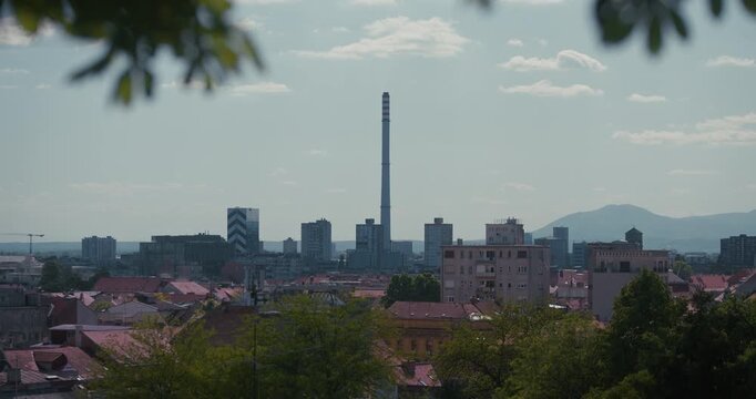 Elevated panoramic view of the Zagreb skyline with residential buildings, modern towers, and an industrial chimney in the distance.