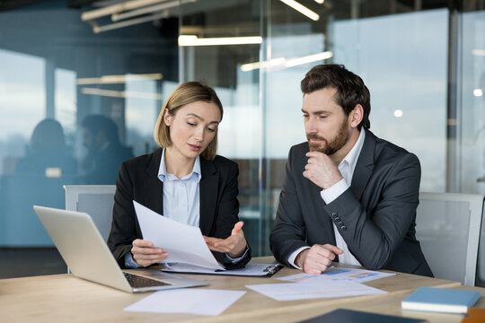 Businesswoman explaining documents to a male colleague as they review reports, analyze charts and plan strategy together in a modern office workspace, focused and collaborative