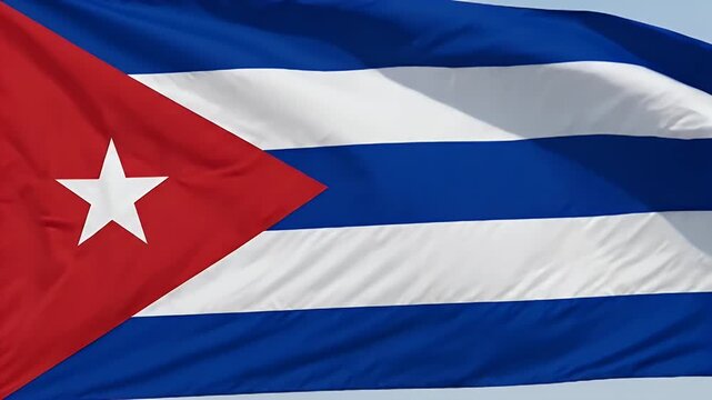 The vibrant Cuban flag waves against a clear sky, showcasing its iconic red triangle with a white star and alternating blue and white stripes.
